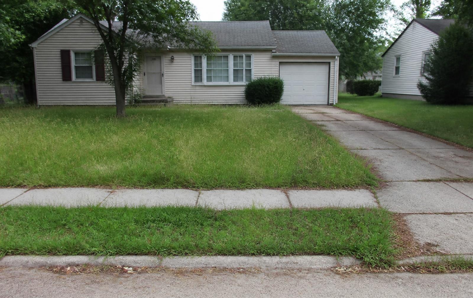 Overgrown, unmaintained front lawn with ragged edges before lawn care